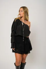 Blusa negra con un hombro descubierto y manga larga con volados.