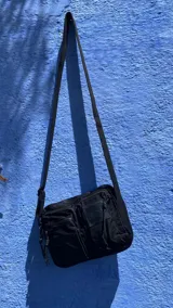 Cartera bandolera negra de nylon con múltiples bolsillos y correa ajustable.