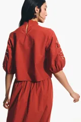 Blusa de viscosa color rojo óxido con secciones de broderie en el pecho y las mangas, cuello elevado festoneado y mangas globo al codo con puños elásticos.