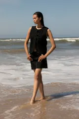 Chaleco de denim celeste sin mangas, confeccionado en algodón. Presenta un cierre frontal con botones forrados en la misma tela y un diseño de bajo redondeado con una abertura central.