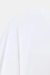 Camiseta blanca de manga corta con corte oversize y cuello redondo. El diseño presenta mangas amplias tipo capa que caen desde el hombro.