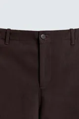 Pantalón de hombre color marrón oscuro, de corte balloon fit, con cintura con trabillas y cierre frontal de botón y cremallera. Presenta bolsillos delanteros y bolsillos traseros de vivo.