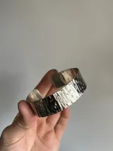 Pulsera brazalete rígido de alpaca plateada con textura irregular hecha a mano.