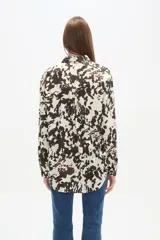 Camisa negra de viscosa con corte holgado, cuello clásico, cierre frontal de botones y detalle de tachas metálicas en la línea de los hombros.