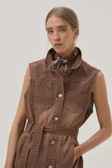 Chaleco largo marrón de algodón con cuello camisero, cierre frontal con botones, bolsillos laterales y lazo ajustable en la cintura.