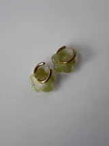 Aros de acero quirúrgico dorados con argolla pequeña y dije colgante en forma de flor de resina color verde claro.