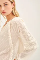 Camisa de manga larga confeccionada en tela plumeti, con cuello redondo, tajo delantero con cordones ajustables y volados verticales en el frente.