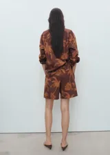 Short de algodón color marrón con estampado de palmeras, diseño recto, pinzas delanteras, bolsillos laterales y cierre con gancho y cremallera.