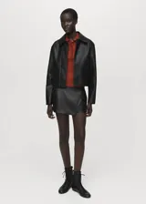 Falda pantalón corta de efecto piel color negro, de tiro medio con diseño cruzado y cierre de cremallera lateral.