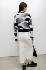 Buzo tejido en técnica jacquard con diseño de formas abstractas en tonos rojos, rosados y violetas. Presenta cuello redondo, mangas largas y puños y ruedo acanalados.