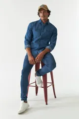 Camisa de jean azul de manga larga con dos bolsillos frontales con solapa abotonada.