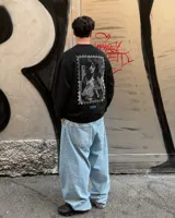 Buzo negro de cuello redondo con estampa en la espalda en formato de estampilla que muestra a una persona sosteniendo un gato.