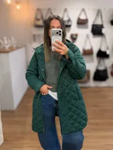Campera larga de diseño capitoneado en color verde, con cierre frontal y botones a presión. Cuenta con capucha y bolsillos laterales, ofreciendo un estilo funcional y abrigado.