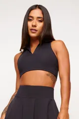 Top deportivo negro, estilo crop top, con cuello polo y escote en V. Presenta tirantes anchos y corte ajustado al cuerpo.