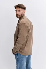 Camisa de pana color tostado, con cuello clásico, cierre frontal de botones y bolsillo en el pecho con etiqueta pequeña.