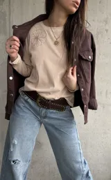 Remera manga larga de color beige, con cuello redondo y diseño bordado de flores en el hombro y lateral.