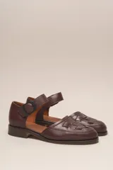 Zapato de cuero color borgoña, con puntera redondeada y diseño trenzado. Presenta una tira sobre el empeine con hebilla metálica negra.