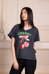 Remera negra con efecto gastado, escote en "v" y estampado frontal de cerezas con moño rosa y texto "Cherry Bomb" en verde.