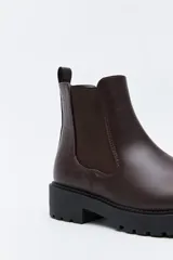 Bota tipo chelsea de caña baja con suela dentada robusta. Presenta un diseño combinado con paneles laterales elásticos, acabado liso en el frente y detalle texturizado en relieve en la parte posterior, incluyendo un tirador trasero para facilitar el calce.