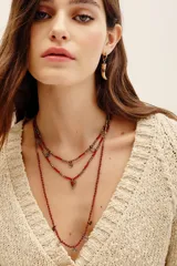 Collar multicapa compuesto por tres tiras de cuentas de vidrio rojas y elementos metálicos dorados, con dijes colgantes incluyendo un dije triangular con piedra roja.