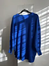 Sweater oversize de tejido liviano, color beige, con cuello redondo, mangas largas con puños acanalados y tajos laterales. Presenta una costura vertical decorativa en el frente y un diseño más largo en la parte posterior.