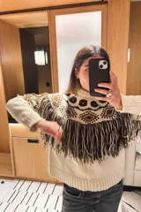 Sweater de lana color crudo con diseño geométrico en color marrón, cuello redondo y detalle de flecos en la parte frontal.