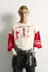 Camiseta boxy fit de cuello redondo y manga por debajo del codo. Presenta un diseño bicolor en tonos blanco off-white y rojo, con estampado y parches frontales con efecto lavado vintage y franjas en las mangas.
