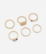 Set de seis anillos en tono dorado con acabado mate, que incluye diseños variados como bandas lisas, una banda texturizada con pequeñas esferas, un anillo con placa circular texturizada y anillos decorados con pequeñas cuentas de resina en colores azul, blanco y marrón.