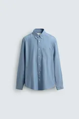 Camisa de corte regular fit confeccionada en tejido chambray de algodón con efecto lavado. Presenta cuello con botones, manga larga con puños abotonados, bolsillo en el pecho y cierre frontal de botones.