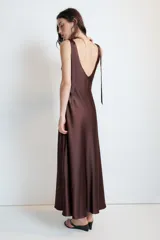 Vestido midi satinado color marrón, con escote en V y tirantes anchos ajustables con lazada en los hombros. Presenta cierre lateral con cremallera oculta.