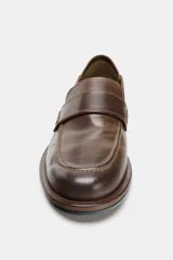 Mocasín de cuero color marrón con diseño de antifaz en el empeine, acabado en punta redonda y suela plana con efecto desgastado.