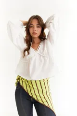 Blusa blanca de algodón con escote en V, mangas largas abullonadas con puños elásticos y diseño con frunces en el frente y la espalda.