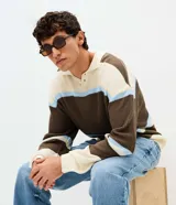 Suéter de punto texturizado con diseño de rayas horizontales en tonos marrón, crema y celeste. Presenta cuello polo con abertura frontal, mangas largas y terminaciones acanaladas en puños y dobladillo.
