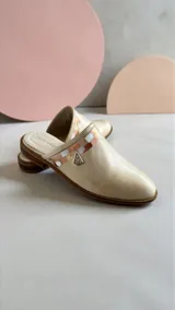 Sandalias cerradas tipo mules de cuero color natural, con detalle de aplique pintado a mano en tonos tierra y herraje metálico triangular en el lateral.