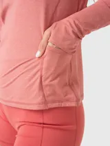 Polera deportiva de manga larga en color rosa melange, con cuello alto y cierre frontal parcial. Presenta un diseño ajustado con costuras visibles y aberturas para los pulgares en los puños.