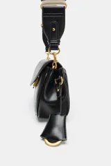 Bolso bandolera de formato alargado en color negro, con solapa frontal y cierre metálico. Incluye una correa ajustable de tejido en color crudo y herrajes dorados.