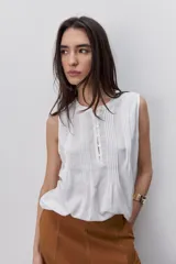 Blusa sin mangas color negro, de silueta fluida, con cuello redondo, detalle de alforzas en el frente y abotonadura parcial con botones visibles.