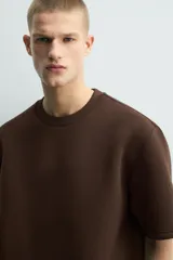 Sudadera de manga corta con corte relajado, confeccionada en tejido técnico compacto de algodón con elasticidad. Presenta cuello redondo y detalle de tacha metálica en la espalda.