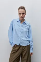 Camisa de viscosa color celeste, de calce amplio y caída fluida, con cuello clásico, cierre frontal de botones y detalles calados en mangas y delantero.
