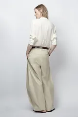 Camisa fluida de cuello redondo y manga larga con puños. Presenta un diseño con pechera frontal, cierre con botones y bajo asimétrico redondeado.