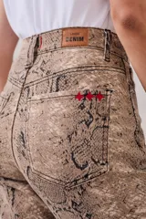 Pantalón de jean de corte recto con estampado de piel de serpiente en tonos beige y marrón. Tiene tiro medio y cierre frontal con botones.