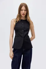 Chaleco largo negro con rayas finas, cuello redondo y cierre frontal de botones. Diseño entallado con bolsillos delanteros ribeteados y abertura en la parte trasera.