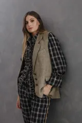 Chaleco sastrero de tweed en tono beige con diseño de espiga. Presenta solapas clásicas, cierre frontal con botones de cuero, bolsillos laterales con tapa y hombreras que definen la silueta. Es una prenda totalmente forrada de corte recto y holgado.