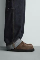 Zueco marrón de piel con acabado serraje, detalle de cinta en el empeine, plantilla acolchada, horma redonda y suela con volumen.