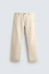 Pantalón de algodón color beige claro, de corte recto (regular fit), con pespuntes en hilo contrastante oscuro. Presenta bolsillos delanteros y bolsillos traseros de parche.