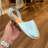 Sandalia tipo avarca color celeste metalizado, con tira trasera y suela plana.