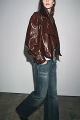 Chaqueta de Zara Woman Collection en tejido con acabado brillante efecto cuero. Presenta cuello solapa, manga larga con trabillas ajustables, bolsillos delanteros y cierre frontal con botones ocultos bajo solapa.