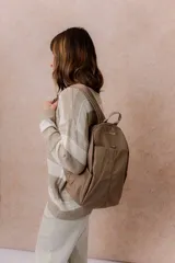 Mochila compacta de color beige, con compartimento principal con cierre, bolsillos laterales y bolsillo frontal con cierre oculto. Cuenta con correas regulables y acolchonadas y asa superior.