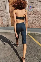 Jeans de tiro medio en denim azul oscuro, con diseño capri de pernera entallada. Presenta cierre frontal con cremallera y botón, y un cinturón integrado con hebilla metálica en la cintura.