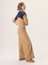 Pantalón de corte ancho y estilo comfy, confeccionado en algodón color marrón. Presenta detalles de franjas verticales en tonos beige y rojo a lo largo de las piernas, con cintura elástica.